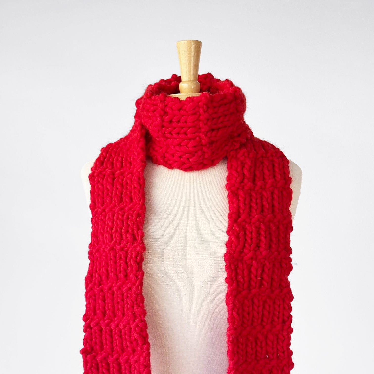 Red knitted scarf displayed on a mannequin.