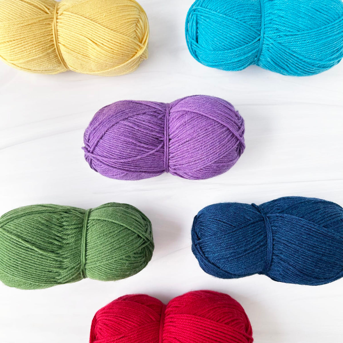 Six skeins of Berroco Ultra Wool yarn in assorted colors arranged on a white background: pale yellow, bright turquoise, lavender purple, sage green, dark navy blue, and red.
