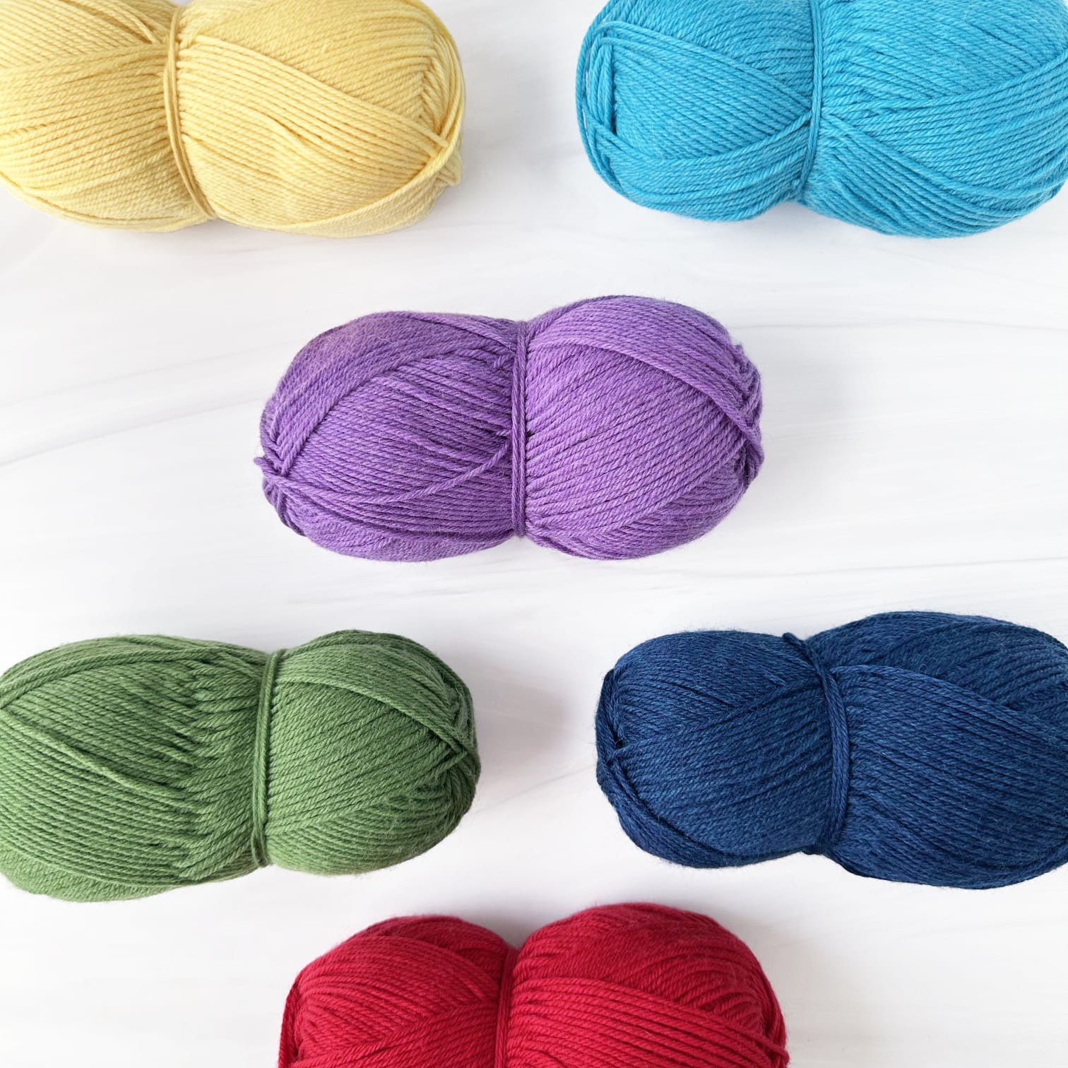 Six skeins of Berroco Ultra Wool yarn in assorted colors arranged on a white background: pale yellow, bright turquoise, lavender purple, sage green, dark navy blue, and red.