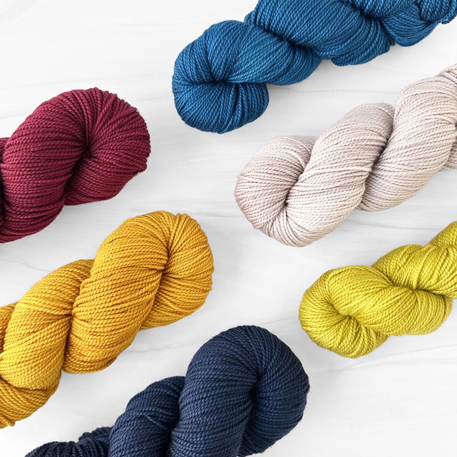 Skeins of Manos del Uruguay Sami yarn in red, blue, tan, chartreuse, navy, and yellow.