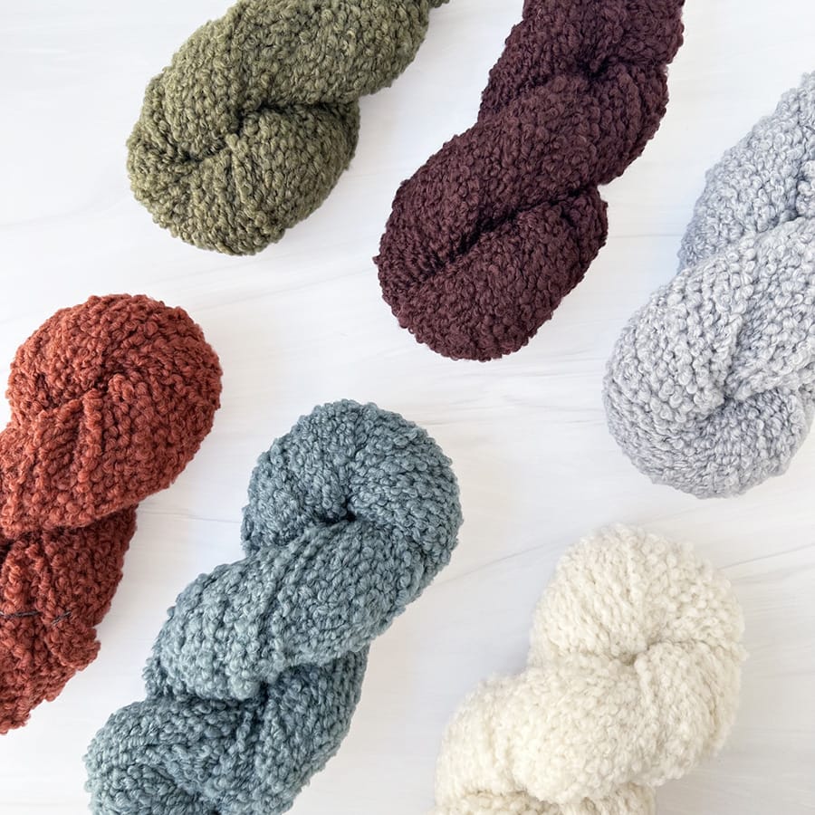 Woolfolk Flette Bulky yarn in olive green, deep plum, rust, blue-green, light gray, and natural white, arranged on a white background.