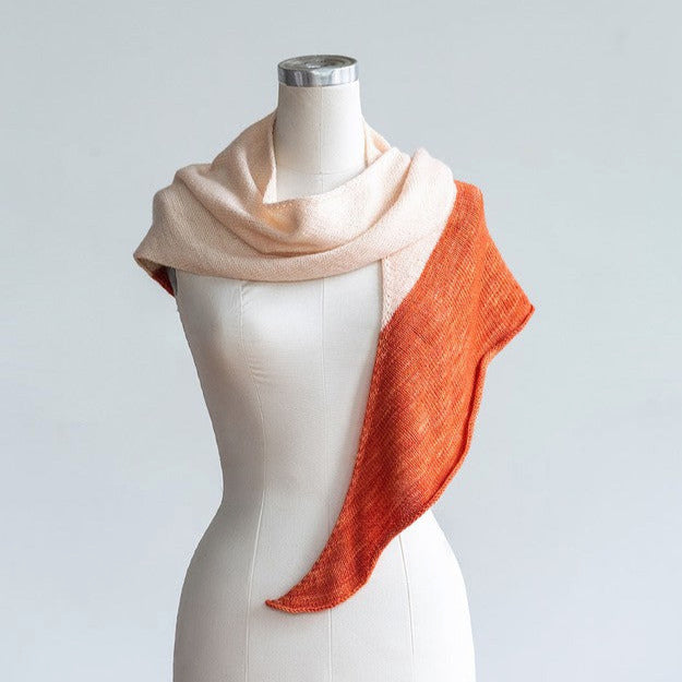 A knitted two-toned shawl in orange and pink colors displayed on a mannequin.